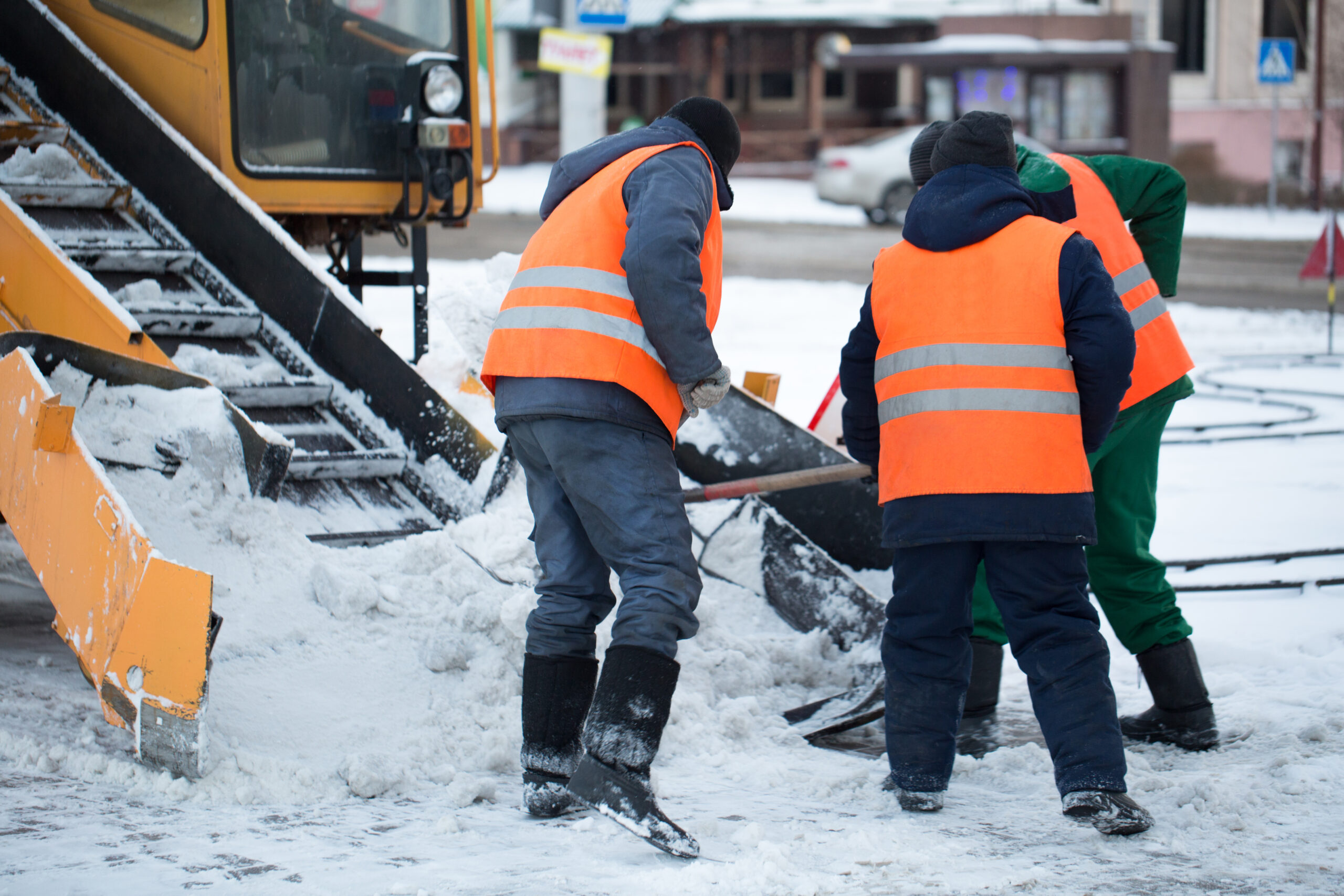 Tractor cleaning the road from the snow. Excavator cleans the streets of large amounts of snow in city. Workers sweep snow from road in winter, Cleaning road from snow storm